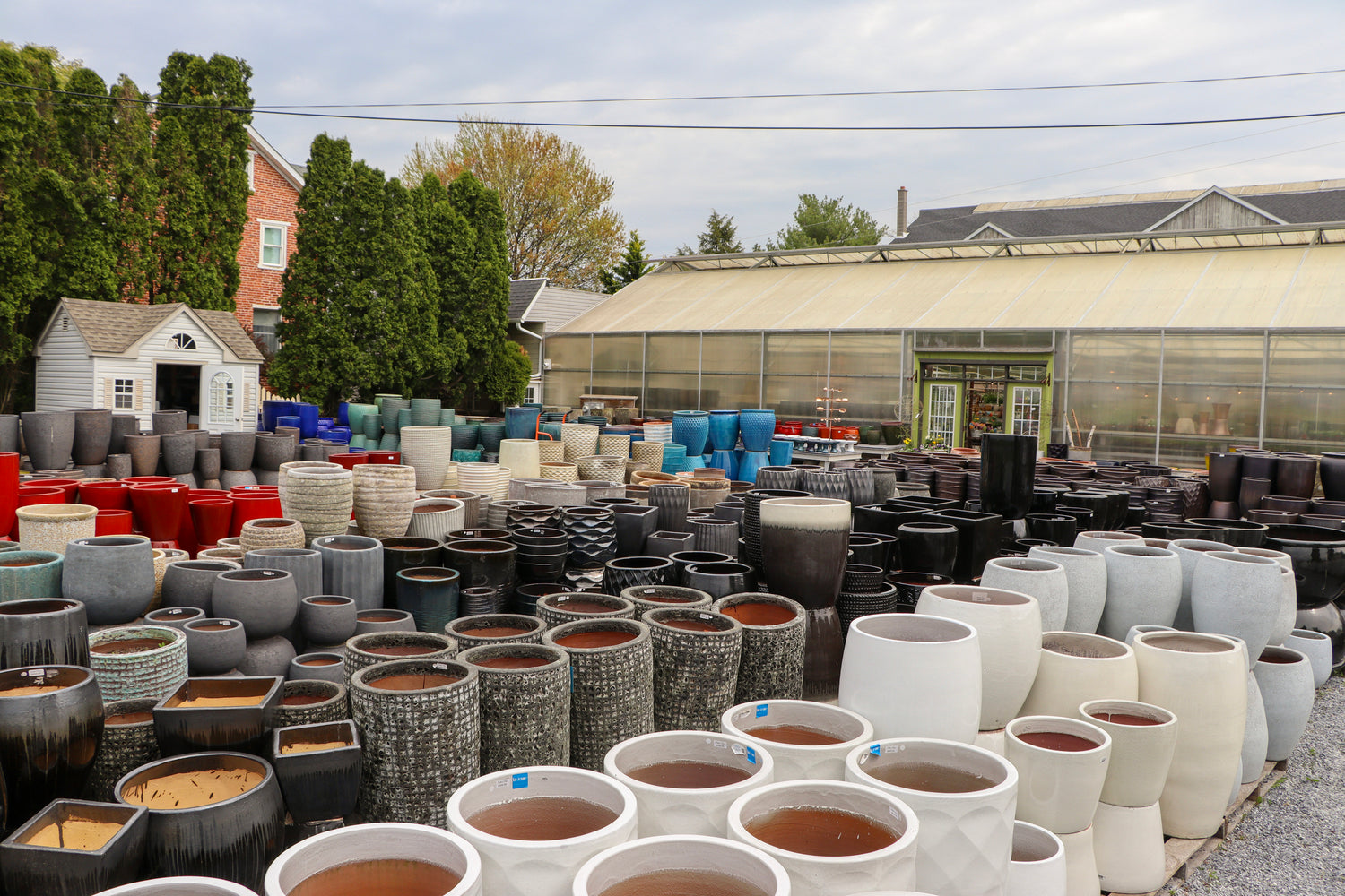 A huge green house behind a massive pottery yard with lots of shapes and sizes of pots.