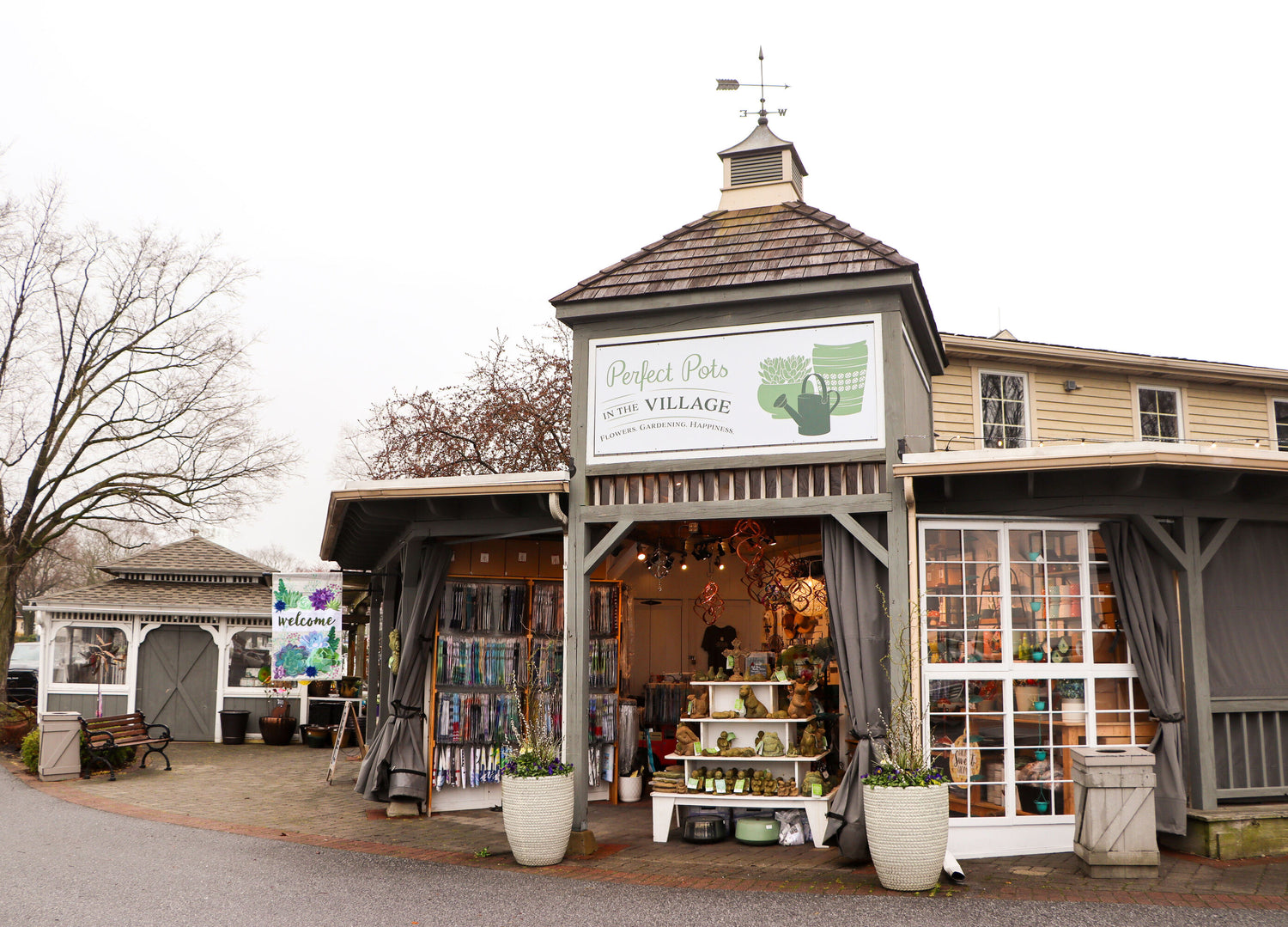 Far away image of Perfect Pots In The Village location, shows flag displays and assorted garden decor.